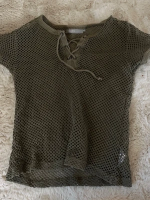 Olivgrön nät-topp med snörning KappAhl - Olivgrön nät-topp från KappAhl med snörning framtill. Toppen är kortärmad och har en luftig mesh-design.💕