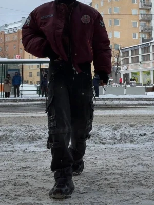 Vinröd bomberjacka med patches - Snygg vinröd bomberjacka med svarta muddar och coola patches på bröstet. Jackan har dragkedja framtill, två fickor med tryckknappar och detaljer som 'H2 AVIATION' och broderad stjärna. Perfekt för dig som vill sticka ut med streetstyle.