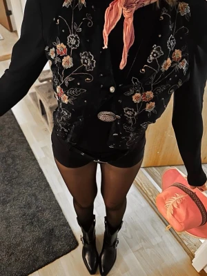 Svarta cowboy boots med spänne - Snygga svarta cowboy boots i glansigt skinn med markerad spetsig tå och dekorativt metallspänne vid ankeln. Klassisk westernstil med hög skaft och robust sula. Knappt använda