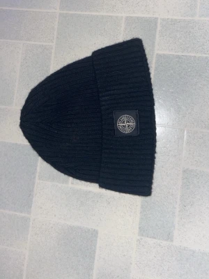  Stone Island mössa, bra skick ny pris 2000 - Svart ribbstickad mössa från Stone Island med uppvikt kant och klassisk logopatch framtill. Snygg och enkel design som passar till det mesta. Perfekt accessoar för kyliga dagar.