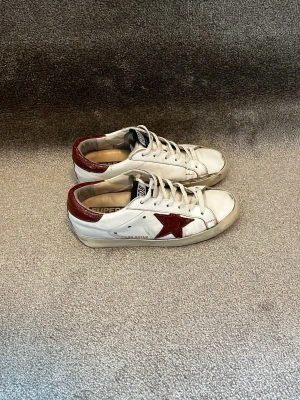 Golden Goose skor - Hej! Säljer dessa Golden Goose skor i vitt läder med vinröda detaljerl. Klassisk låg modell med vita snören och slitna detaljer. Handgjorda I italien och kostar runt 6000kr nya. Rätt så slitna sulor men man kan få det fixat hos skomakare för den som har lust att göra det. Storlek 36