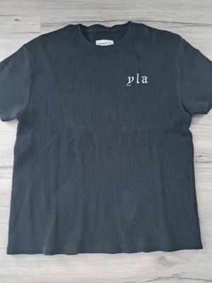 Svart  t-shirt från YoungLA - Svart t-shirt från YoungLA med ribbad struktur och tryck i vitt framtill och baktill. Klassisk rund halsringning och korta ärmar. Perfekt för en avslappnad och trendig stil.