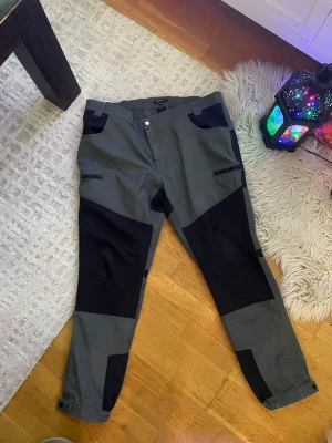 Grå och svarta cargopants - Snygga cargopants i grått och svart med flera fickor och förstärkta partier på knän och bak. Byxorna har en avslappnad passform och justerbara benslut. Perfekta för dig som gillar en streetwear-look.