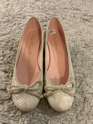 Beige ballerinaskor Pretty Ballerinas - Snygga beige ballerinaskor från Pretty Ballerinas med låg klack och ormskinnsmönster. Skorna har en dekorativ rosett framtill och glittriga detaljer som ger extra stil. Insidan är ljusrosa och materialet känns lyxigt och trendigt.