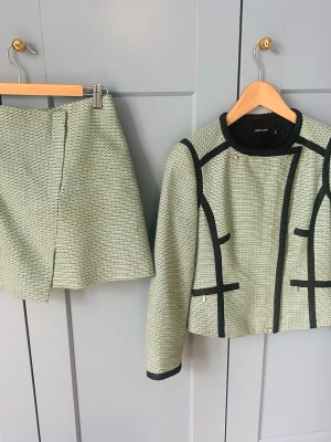 Turkosgrön/beige kavaj och kjol från Karen Millen - Snyggt set från Karen Millen med turkosgrön/beige kavaj och matchande kjol. Kavajen har svarta detaljer, rund halsringning och dekorativa fickor. Kjolen är rak med liten slits fram. Båda delar har ett diskret mönster och känns klassiska men trendiga.