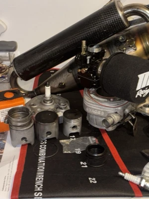 Mk2 70 - Säljer ett paket med motordelar till moped, inklusive cylinder, kolvar, tändstift, förgasare och ett avgassystem med kolfiberljuddämpare. Perfekt för dig som gillar att meka och vill uppgradera eller laga din moped. Flera delar i metall och kolfiber.