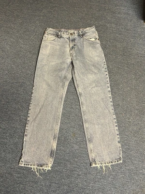 Ljusblå raka jeans från Wrangler - Ljusblå jeans från Wrangler med rak passform och klassisk femficksdesign. Jeansen har råa, fransiga benslut för en avslappnad vibe. Tillverkade i denim med vintagekänsla och knappgylf. Perfekta för dig som gillar en retrostil.