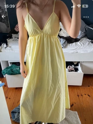 Ljusgul ärmlös klänning med v-ringning - Söt ljusgul klänning med smala axelband och djup v-ringning. Klänningen har en luftig passform och faller mjukt ner till vaden. Perfekt för varma dagar och enkel att styla med accessoarer.