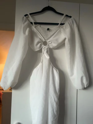 Vit klänning med ringdetalj - Trendig vit klänning med ballongärmar och snygg ringdetalj framtill. Klänningen har offshoulder-design och smockad rygg för skön passform. Perfekt för sommarens alla tillfällen och ger en riktigt fräsch look.