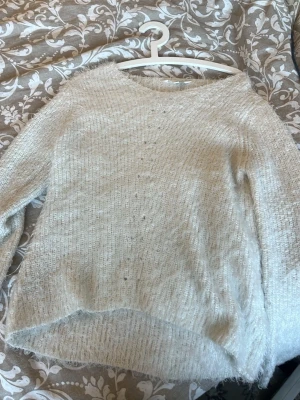 Vit fluffig stickad tröja - Mysig vit stickad tröja med fluffig känsla och diskreta små hål framtill. Tröjan har v-ringning  och långa ärmar. Perfekt för dig som gillar en enkel men ändå lite extra look. S/M