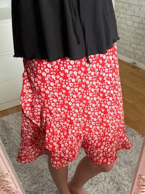 Röd blommig kjol från Seaside - Supersöt röd kjol från Seaside med vitt blommönster och volangkant. Kjolen har en avslappnad passform och resår i midjan. Perfekt för dig som vill ha en färgglad och sommrig outfit.