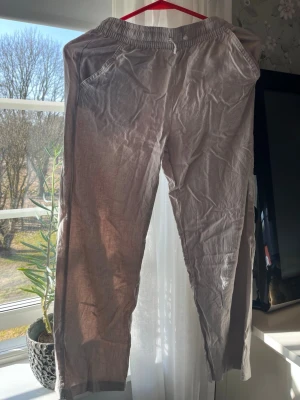 Beige linnebyxor med resårmidja - Snygga beige linnebyxor med avslappnad passform och resår i midjan. Byxorna har två sidofickor och är tillverkade i ett lätt och luftigt linnematerial, perfekta för en chill och stilren look.