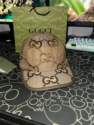 Beige Gucci keps  - Säljer en beige keps från Gucci med klassiskt GG-mönster i brunt. Kepsen har böjd skärm och är tillverkad i canvas med detaljer i läder. Insidan är ljus och har Gucci-etikett. Perfekt för dig som vill ha en lyxig accessoar.
