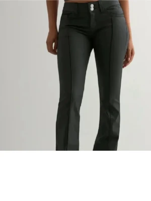 Svarta bootcut jeans från Nelly - Snygga svarta bootcut jeans från Nelly med låg midja och markerade sömmar framtill. Jeansen har två knappar i midjan och klassiska bakfickor med dekorativa sömmar. Perfekta för en trendig och stilren look.