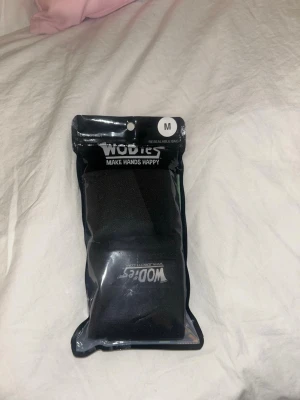 Svarta träningsskydd från WODies - Säljer ett par svarta träningsskydd från WODies, perfekta för crossfit eller styrketräning. De har tre hål för fingrarna och är tillverkade i ett stretchigt och slitstarkt material som ger bra grepp och skydd för händerna under tuffa pass. Skriv gärna vid frågor!☺️