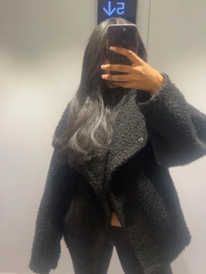 Svart oversized teddyjacka, Ginatricot - Säljer en svart teddyjacka med oversized passform och bred krage.  Perfekt till våren. Jackan har ett mjukt bouclé-material och stora ärmar som ger en cool och avslappnad look. Perfekt för dig som gillar trendiga och bekväma ytterplagg.