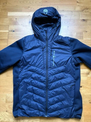 Marinblå vindjacka från Sail Racing - Snygg marinblå vindjacka från Sail Racing med huva och dragkedja framtill. Jackan har två sidofickor med dragkedja och en bröstficka, samt logga på bröstet. Materialet är lätt och vindtätt, perfekt för blåsiga dagar. Jag har använda jackan i ca ett halvår, dock så kände slutade jag använda då den börjat bli för liten. Jackan är i storlek M och funkar året om speciellt under våren. Hör av dig vid intresse!