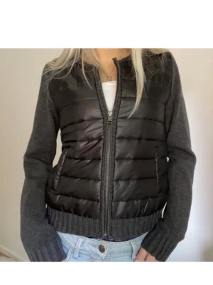 Svart pufferjacka med stickade ärmar - har storlek xs och s Snygg svart pufferjacka med quiltad front och rygg i glansigt material samt stickade mörkgrå ärmar och muddar. Jackan har dragkedja framtill och två fickor. Perfekt för kalla dagar när du vill ha både stil och värme.