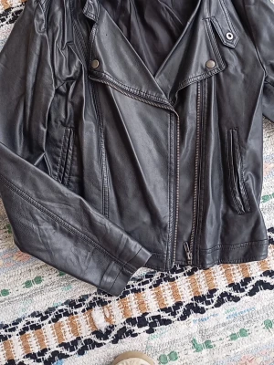 Svart skinnjacka från Bik Bok Large  - Snygg svart skinnjacka från Bik Bok med klassisk bikerkrage, sned dragkedja och två fickor framtill. Jackan har detaljer i silver och en cool, tidlös look som passar perfekt till jeans eller klänning.