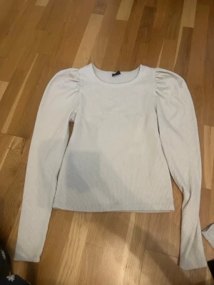 Beige  ribbad topp med puffärm - Snygg vitbegie ribbad topp med långa puffärmar och rund halsringning. Materialet är mjukt och stretchigt, vilket gör den bekväm att bära. 