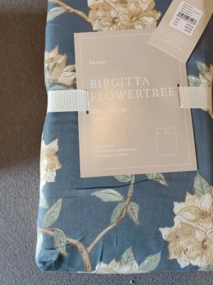 Birgitta Flowertree påslakanset blå från HEMTEX  - Säljer ett Birgitta Flowertree påslakanset från Kid Interiør i färgen mist blue. Setet är i 100% bomull och har ett blommigt mönster i beige och grönt. Innehåller två örngott och ett påslakan. Perfekt för att ge sovrummet en fräsch och stilren känsla. Säljs för 650:- 