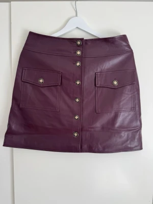 Orsay vinröd mini kjol, storlek 38 - Kort kjol med knappar framtill och två fickor med lock. Knapparna är guldfärgade med svarta detaljer. Kjolen har en rak passform och slutar ovanför knät. Length: 47 cm  Buy shipping label or pick it up from Farsta Centrum in Stockholm.