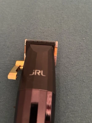 JRL hårtrimmer i svart och guld - Snygg hårtrimmer från JRL i svart och guld med metalliska detaljer. Ergonomiskt handtag och justerbar spak på sidan. Perfekt för att fixa frisyren hemma eller på resan. Klipphuvud i metall för precision.