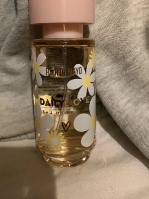 Daily Love parfym från Flor de Mayo - Söt parfymflaska med blommigt motiv från Flor de Mayo. Flaskan är genomskinlig med vita och gula prästkragar och har ett ljusrosa lock. Doften heter Daily Love och är en eau de parfum. Perfekt för dig som gillar blommiga och fräscha dofter.