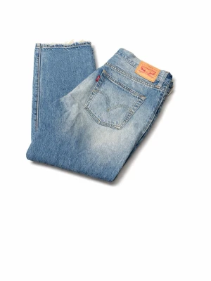 Levi's ljusblå vintage jeans - Säljer ett par klassiska ljusblå Levi's jeans med vintagekänsla. Jeansen har raka ben, fem fickor och den ikoniska röda Levi's-lappen på bakfickan. Materialet är slitstark denim i 100% bomull och passformen är relaxed fit. Storlek 31:32 