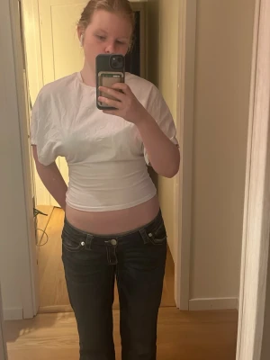 Vit  t-shirt med lösa armar - Säljer en enkel vit croppad t-shirt med lösa, korta ärmar. T-shirten har en klassisk rund halsringning och är gjord i mjukt bomullsmaterial. 