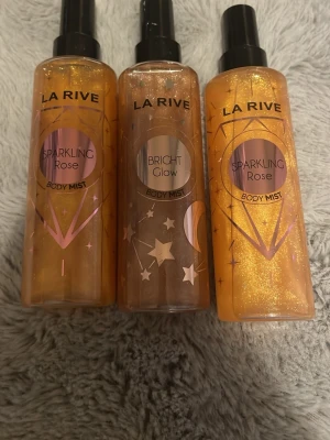 La Rive Body Mist Sparkling Rose & Glow - Tre body mist från La Rive i dofterna Sparkling Rose och Bright Glow. Flaskorna är genomskinliga med skimrande guldigt innehåll och svarta spraymunstycken. Designen har rosa och guldiga detaljer samt stjärnor och månar på Bright Glow. kontakta mig vilken ni vill vill köpa en kostar 30kr och alla tre kostar 80kr