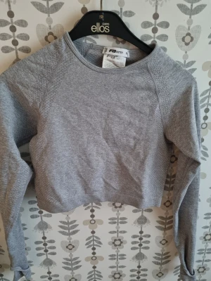 Grå croppad sweatshirt från Puma - Snygg grå croppad sweatshirt från Puma med rund halsringning och långa ärmar. Perfekt för en avslappnad och sportig stil. Mjuk bomullsblandning och ribbade muddar vid ärmslut och nederkant.