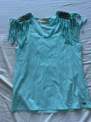 Turkos topp med fransar och paljetter - Snygg turkos topp från Lofty Manner med fransar och paljettdetaljer på axlarna. 