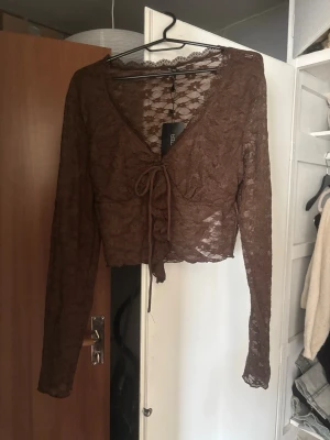 Brun spetsblus med knyt framtill - .Jättesnygg brun långärmad topp i genomskinlig spets med knytning fram. Aldrig använd, lappen sitter kvar! Perfekt för utgång eller till ett par high waisted jeans. 
