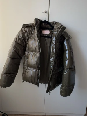 Glansig olivgrön pufferjacka Nelly - Den virala jackan ifrån Nelly. Snygg olivgrön pufferjacka från Nelly med glansig finish och huva. Jackan har dragkedja framtill och är vadderad för extra värme. Perfekt för kalla vinterdagar och ger en trendig look. Använd max 5 gånger💓
