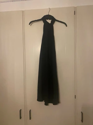 Svart miniklänning med halterneck - Säljer en elegant svart långklänning med halterneck och vid kjol. Klänningen har en stilren och enkel design som ger ett klassiskt intryck. Materialet känns mjukt och faller snyggt. Perfekt för dig som vill ha en tidlös look.