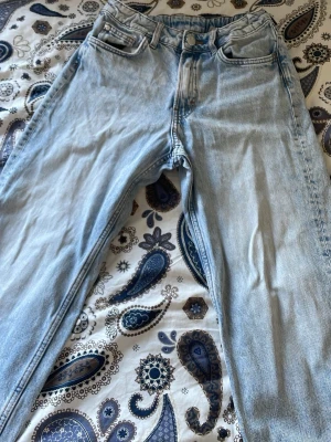 Ljusblå raka jeans - Säljer ett par ljusblå jeans med rak passform och klassiska fem fickor. Jeansen har en knappstängning och dragkedja framtill. Materialet är denim och färgen är snyggt tvättad ljusblå. Perfekt för dig som gillar en avslappnad stil.