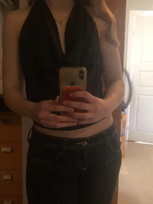 Svart halterneck topp - Snygg svart omlott halterneck topp med djup urringning och croppad passform. Tunt, mjukt material som faller snyggt och ger en elegant look. Perfekt att styla med jeans eller kjol för en trendig outfit.