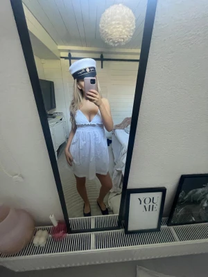 Vitklännning STUDENTKLÄNNING  - Söt vit kort klänning med smala axelband och v-ringning. Klänningen har fina detaljer under bysten upptill och en luftig kjol, perfekt för student eller sommar. 