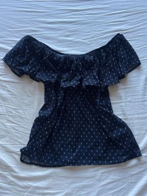 Svart offshoulder blus med volang - Snygg svart offshoulder blus med volangkant och små vita prickar. 