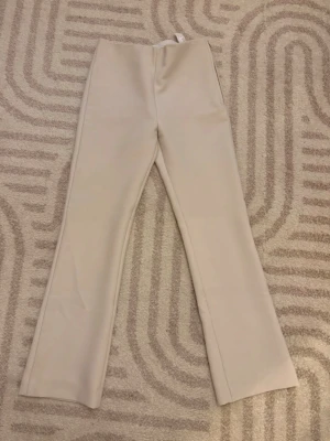 Beige kostymbyxor med raka ben - Snygga beige kostymbyxor med hög midja och raka ben. Byxorna har minimalistisk design utan synliga fickor fram och diskreta fickor bak. Perfekta för en clean och stilren look. Materialet ser ut att vara mjukt och något stretchigt.