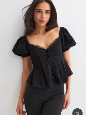 Svart blus med puffärm och spets - Supersnygg svart blus med puffärmar, v-ringning med spetskant och knappar framtill. Blusen har en lätt utsvängd passform och är perfekt för dig som gillar trendiga detaljer och romantisk stil. Använd en gång