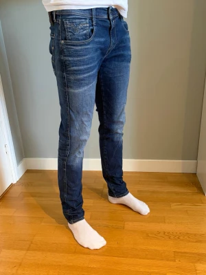 Replay anbass slim fit  - Säljer ett par mörkblå slim fit jeans med klassisk femficksdesign och snygga slitningar. Jeansen har normal midja och smal passform hela vägen ner. Perfekta till en avslappnad stil och passar till det mesta i garderoben. Är 185 och sitter bra