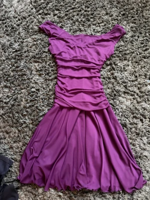 Lila offshoulder klänning Le Chateau - Säljer en lila offshoulder klänning från Le Chateau med figurnära överdel och vidd i kjolen. Klänningen har fina rynkdetaljer.