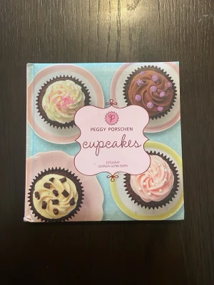 Cupcakes av Peggy Porschen - En färgglad och inspirerande bok om cupcakes av Peggy Porschen. Omslaget pryds av fyra olika cupcakes på pastellfärgade fat. Boken har hårda pärmar och är utgiven av Tukan förlag. Perfekt för dig som älskar bakning och söta bakverk.
