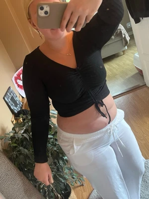 Svart croppad topp med snörning - Säljer en svart croppad topp med lång ärm och v-ringning. Toppen har snygg snörning framtill som ger en cool detalj och sitter tight mot kroppen. Perfekt till höga byxor eller kjol för en trendig look.