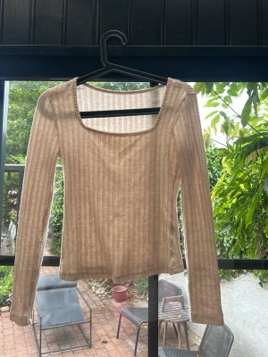 Beige ribbad långärmad topp - Trendig beige långärmad topp med ribbad struktur och fyrkantig ringning. Tillverkad i ett tunt, stretchigt material som ger en snygg passform. Perfekt att styla med jeans eller kjol för en enkel men snygg look.