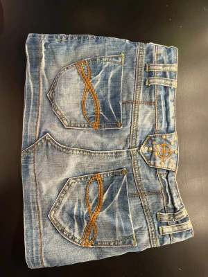Blå vintage jeanskjol med bruna och guldiga detaljer - Strl XXS från fishbone, brun broderi på bakfickorna och guldiga nitar, säljer då den inte kommer till användning💓 Köpt second hand men har inga defekter 