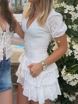 Meet me there student klänning - 799kr nypris. Söt vit kortklänning med broderade detaljer och volanger. Klänningen har v-ringning, puffärmar och omlottkänsla upptill. Perfekt för sommarens alla tillfällen och ger en romantisk vibe. 