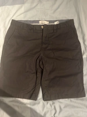 Svarta linneshorts från Dressmann - Svarta shorts från Dressmann i en skön linneblandning. Klassisk rak modell med fickor på sidorna och knappstängning i midjan. Perfekta för varma dagar när du vill ha en stilren och enkel look.